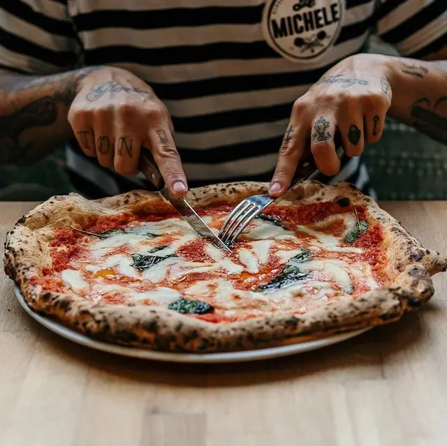 Am Bild zu sehen sind 2 Männerhände, die gerade eine Pizza (Margherita) schneiden.
