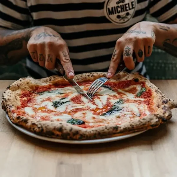 Am Bild zu sehen sind 2 Männerhände, die gerade eine Pizza (Margherita) schneiden.